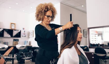 Female hair stylist working on a woman 's hair. Woman hairdresser serving her customer at the salon. - JLPSF01583