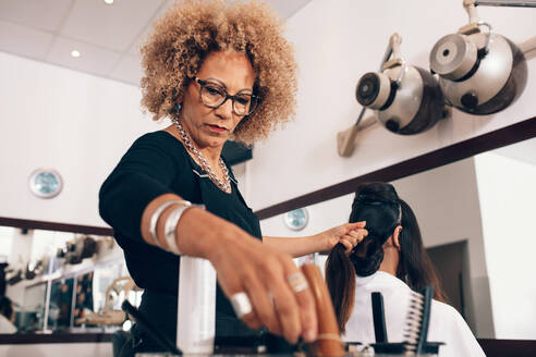 Friseurin bei der Arbeit an den Haaren einer Frau. Ältere Friseurin bei der Herstellung einer stilvollen Frisur. - JLPSF01584