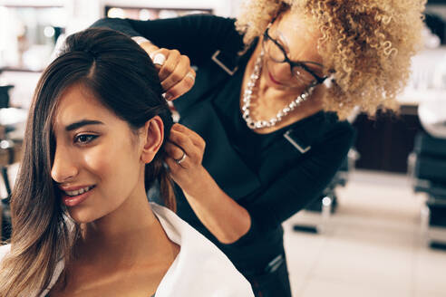 Nahaufnahme einer Frau, die sich im Salon eine elegante Frisur machen lässt. Professionelle Haarstylisten stecken das Haar auf elegante Weise hoch. - JLPSF01588