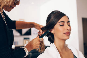 Woman hairdresser using a hairbrush for a hairdo at the salon. Young woman getting a stylish hairdo done at salon. - JLPSF01589