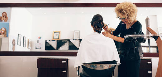 Hairdresser styling the hair of a customer at salon. Female hair stylist setting hair in fashionable design using a comb. - JLPSF01592