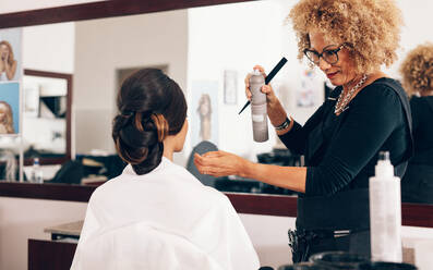 Friseurin, die ein Haarfestigungsspray zum Stylen der Haare verwendet. Weibliche Friseurin, die im Salon die Haare in ein modisches Design bringt. - JLPSF01594