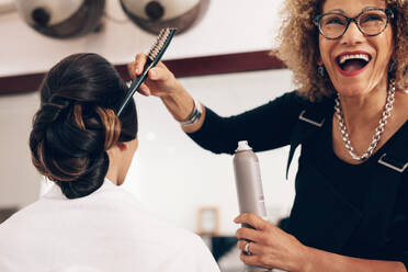 Ältere Frau Friseurin hält ein Haar Einstellung Spray und eine Bürste im Salon. Friseurin in einer glücklichen Stimmung bei der Arbeit im Salon. - JLPSF01595