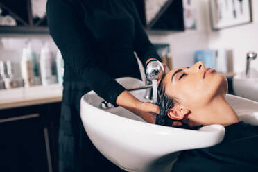 Nahaufnahme eines Friseurs, der einer Kundin im Salon die Haare wäscht. Frau, die im Friseursalon eine Wellness-Behandlung erhält - JLPSF01597