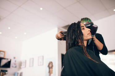Friseurin mit Gebläse und Bürste zum Trocknen der Haare. Frau in einem eleganten Schönheitssalon, die eine Frisur bekommt. - JLPSF01606