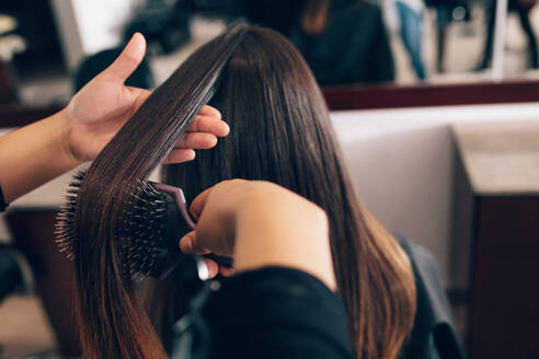 Professioneller Friseur, der einer Kundin im Salon die Haare stylt. Friseurin kämmt die Haare mit einer Haarbürste. - JLPSF01609