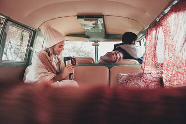 Friends on road trip travelling by camper van. Woman sitting in back seat of van with man driving. - JLPSF01620