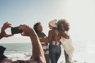 Ein Mann fotografiert schöne Frauen am Strand. Freundinnen posieren für ein Foto im Freien während ihres Roadtrips. - JLPSF01652