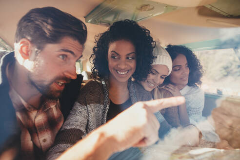 Freunde auf einem Roadtrip, die in einem Van sitzen und eine Landkarte als Wegweiser benutzen, eine Gruppe von Männern und Frauen, die zusammen reisen. - JLPSF01661