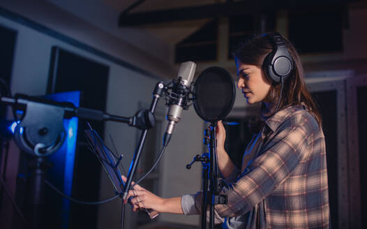 Frau nimmt Musik in einem professionellen Aufnahmestudio auf. Sängerin mit Kopfhörern liest Texte. - JLPSF01665