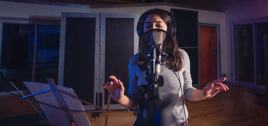 Young music artist singing a song in the recording studio. Female singer in front of microphone. - JLPSF01666