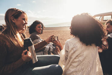 Freunde auf einem Roadtrip, die nach der Reise eine Pause einlegen. Eine Gruppe von Männern und Frauen sitzt im Freien und trinkt Kaffee. - JLPSF01667