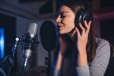 Close up of female vocal artist singing in a recording studio. Woman playback singer singing a song. - JLPSF01671