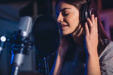Female singer in front of microphone. Young music artist singing a song in the recording studio. - JLPSF01672
