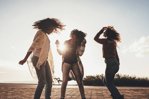 Freundinnen tanzen und amüsieren sich an einem sonnigen Tag auf der Straße. Drei junge Frauen genießen ihren Roadtrip. Freundinnen, die sich im Urlaub amüsieren. - JLPSF01680