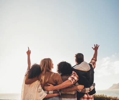 Vier Freunde stehen mit erhobenen Armen zusammen, eine Gruppe von Männern und Frauen, die sich im Urlaub vergnügen. - JLPSF01682