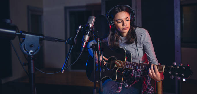 Sängerin, die ein Lied im Studio vorträgt und Gitarre spielt. Sängerin, die in einem Aufnahmestudio Gitarre spielt. - JLPSF01688