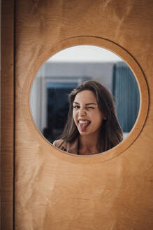 Junge Geschäftsfrau streckt die Zunge heraus, gesehen durch Glas - JOSEF13401