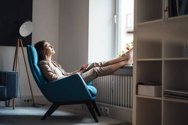 Businesswoman relaxing on chair at home - JOSEF13402