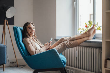 Happy businesswoman with feet up sitting on chair at home - JOSEF13414