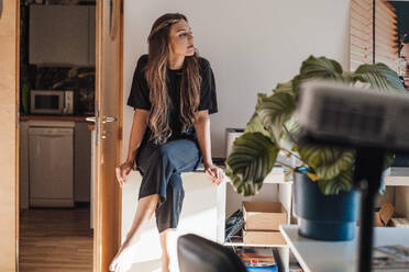Nachdenkliche junge Frau mit langen Haaren sitzt zu Hause am Tisch - JOSEF13432