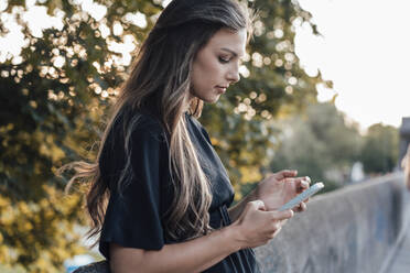 Young woman in long hair using mobile phone by wall - JOSEF13478