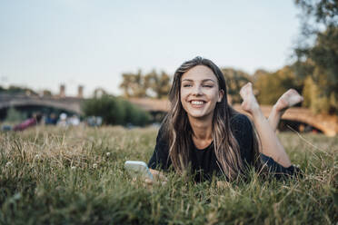 Glückliche Frau mit Smartphone im Gras liegend im Park - JOSEF13485