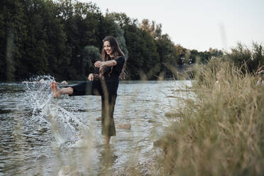 Happy young woman splashing water in lake - JOSEF13488