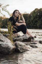 Nachdenkliche junge Frau sitzt am See - JOSEF13497