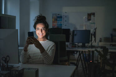 Lächelnde Geschäftsfrau mit Mobiltelefon am Schreibtisch im Büro - JOSEF13510