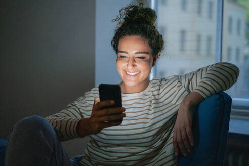 Glückliche Frau, die ein Smartphone auf einem Stuhl im Büro benutzt - JOSEF13511