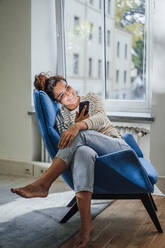 Smiling woman using mobile phone on chair at home - JOSEF13535