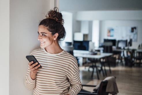 Lächelnde Geschäftsfrau mit Mobiltelefon im Büro - JOSEF13550