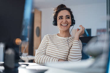 Smiling businesswoman talking through headset in office - JOSEF13554