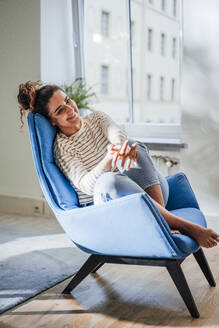 Lächelnde Frau, die auf einem blauen Stuhl zu Hause nachdenkt - JOSEF13591