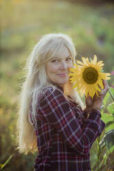 Lächelnde reife Frau hält Sonnenblume an einem sonnigen Tag - AANF00355