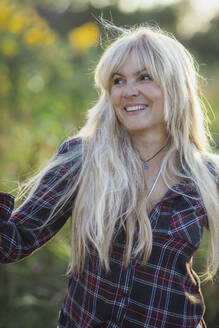 Glückliche blonde Frau mit langen Haaren an einem sonnigen Tag - AANF00356
