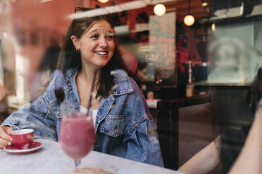 Glückliche Frau im Gespräch mit lesbischer Freundin in einem Café, gesehen durch ein Fenster - ASGF02901