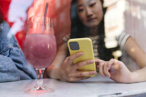 Frau benutzt Smartphone bei einem Glas auf dem Tisch in einem Café - ASGF02909