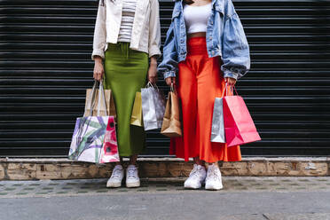 Lesbian couple holding shopping bags in front of shutter - ASGF02916