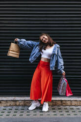 Lächelnde Frau mit Einkaufstüten vor einem Fensterladen - ASGF02921