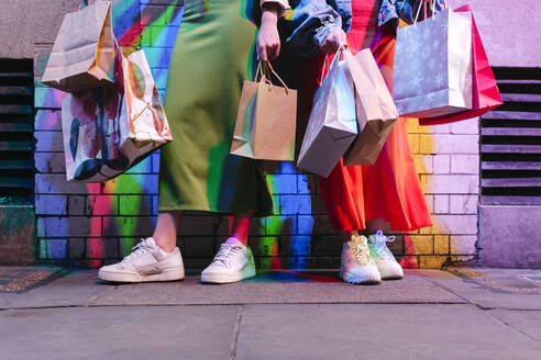 Lesbische Freundinnen halten Einkaufstüten vor einer Backsteinmauer - ASGF02927