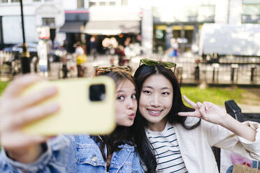 Woman showing peace sign taking selfie with lesbian friend through smart phone - ASGF02934