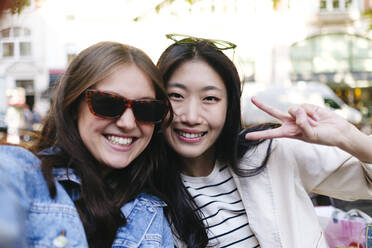 Happy woman wearing sunglasses taking selfie with lesbian friend showing peace sign - ASGF02936