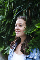 Smiling young woman amidst green plants - ASGF02951