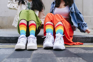 Lesbian women wearing multi colored socks sitting on footpath - ASGF02964