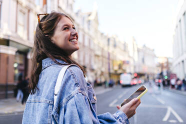 Happy woman with smart phone strolling in city - ASGF02987