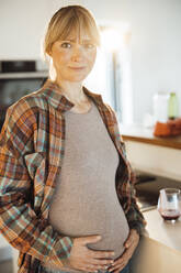 Lächelnde Frau berührt schwangeren Bauch zu Hause - JOSEF13604