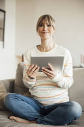 Lächelnde schwangere Frau mit Tablet-PC im Schneidersitz auf dem Sofa - JOSEF13622