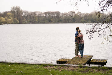 Affectionate couple looking at lake standing on jetty - JOSEF13637